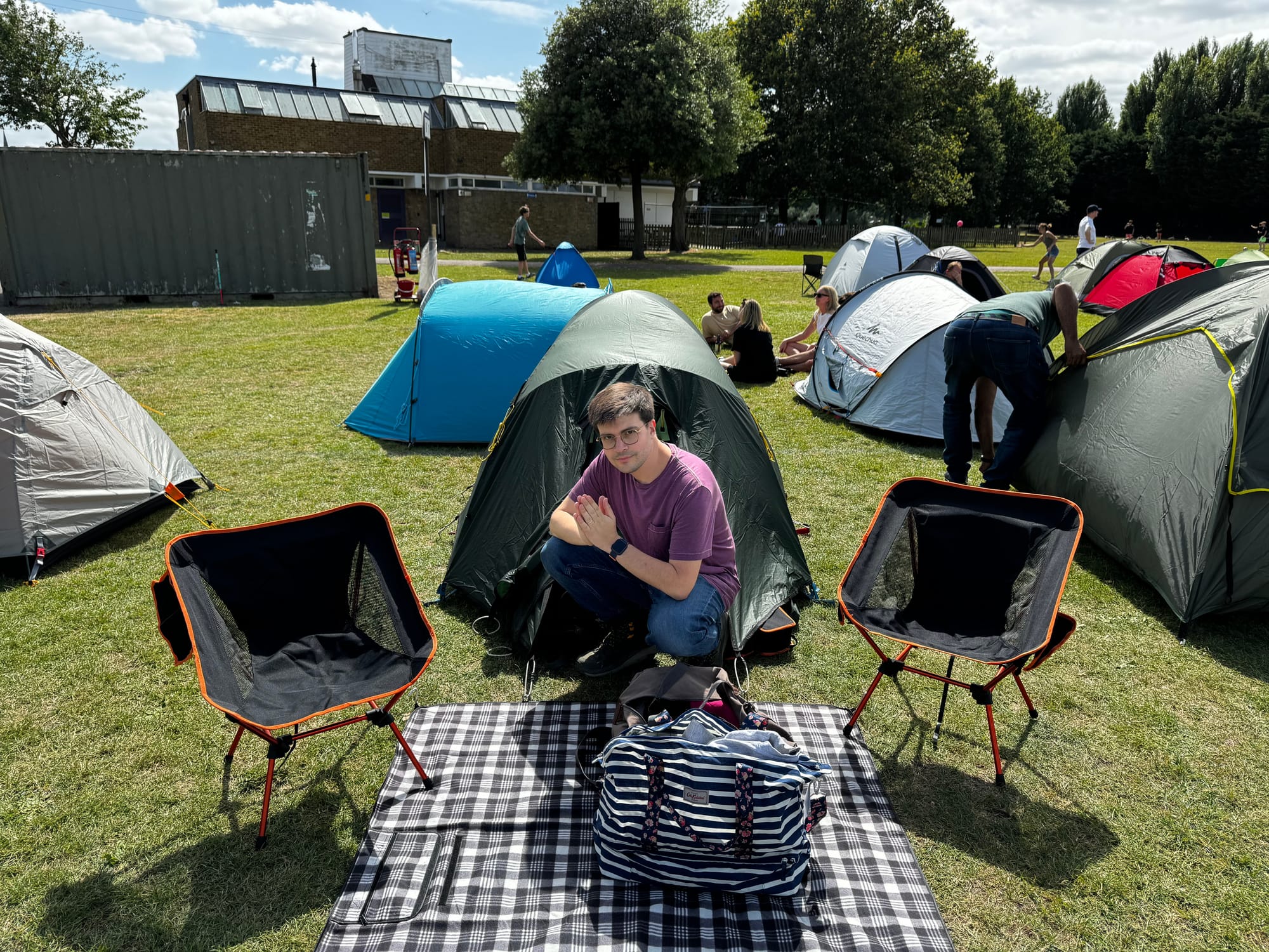 The author kneels in front of a small tent. Two camping chairs flank him.