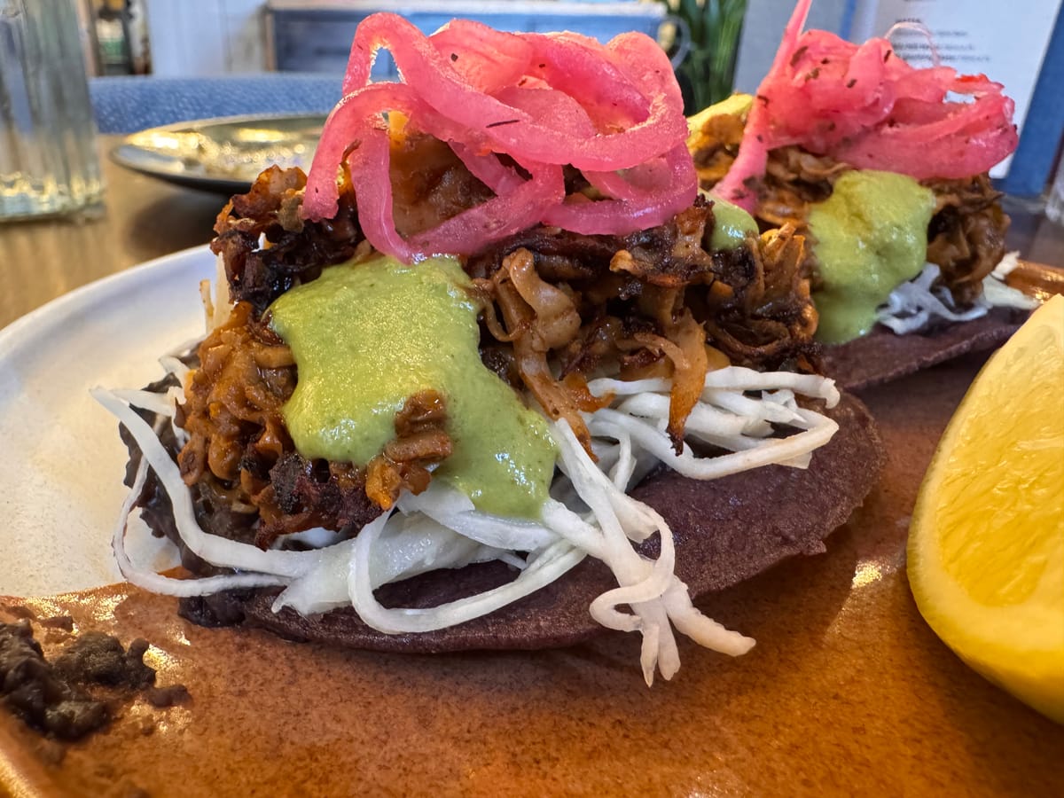 Close-up of a tortilla with pulled mushrooms simulating the look and texture of carnitas, along with other ingredients.