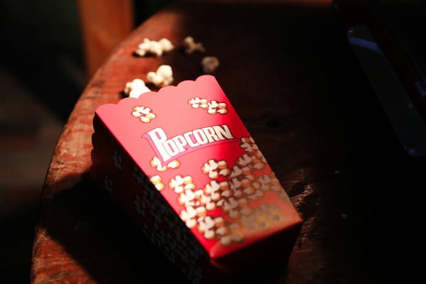 A medium-sized movie popcorn bucket sits on its side, post-spill, as popped corn emanates outwards.